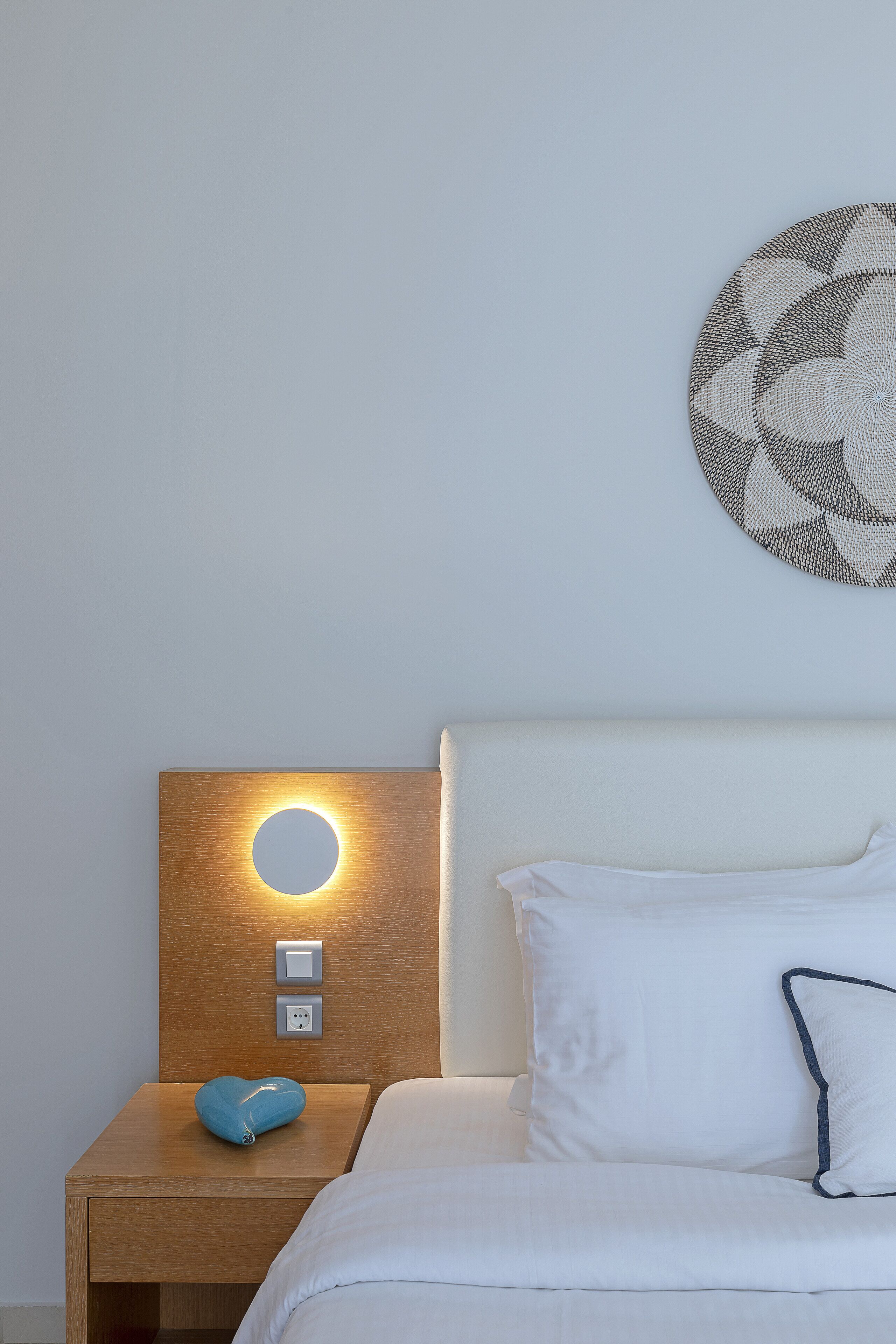 Un dormitorio ordenado con cama, mesita de noche con lámpara y una obra de arte en la pared.