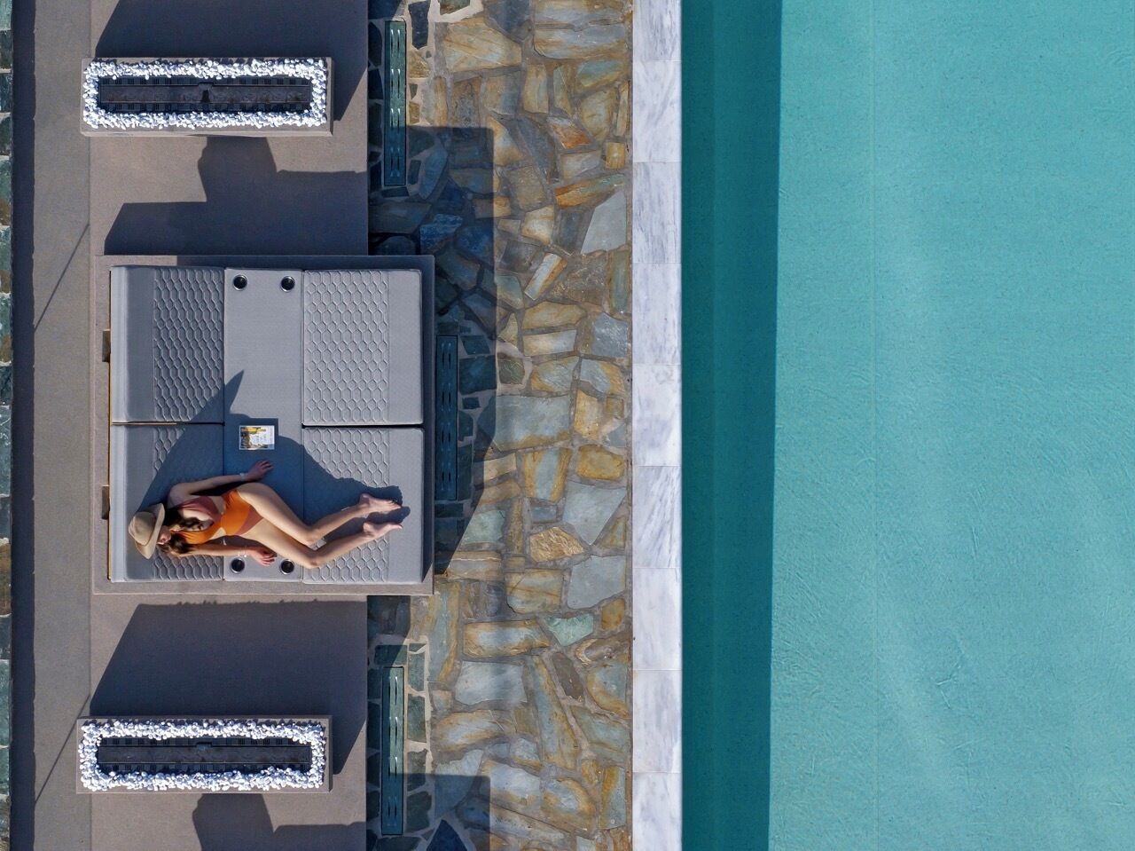 Vue aérienne d’un espace autour d’une piscine, avec des chaises longues et une personne allongée sur l’une d’elles.