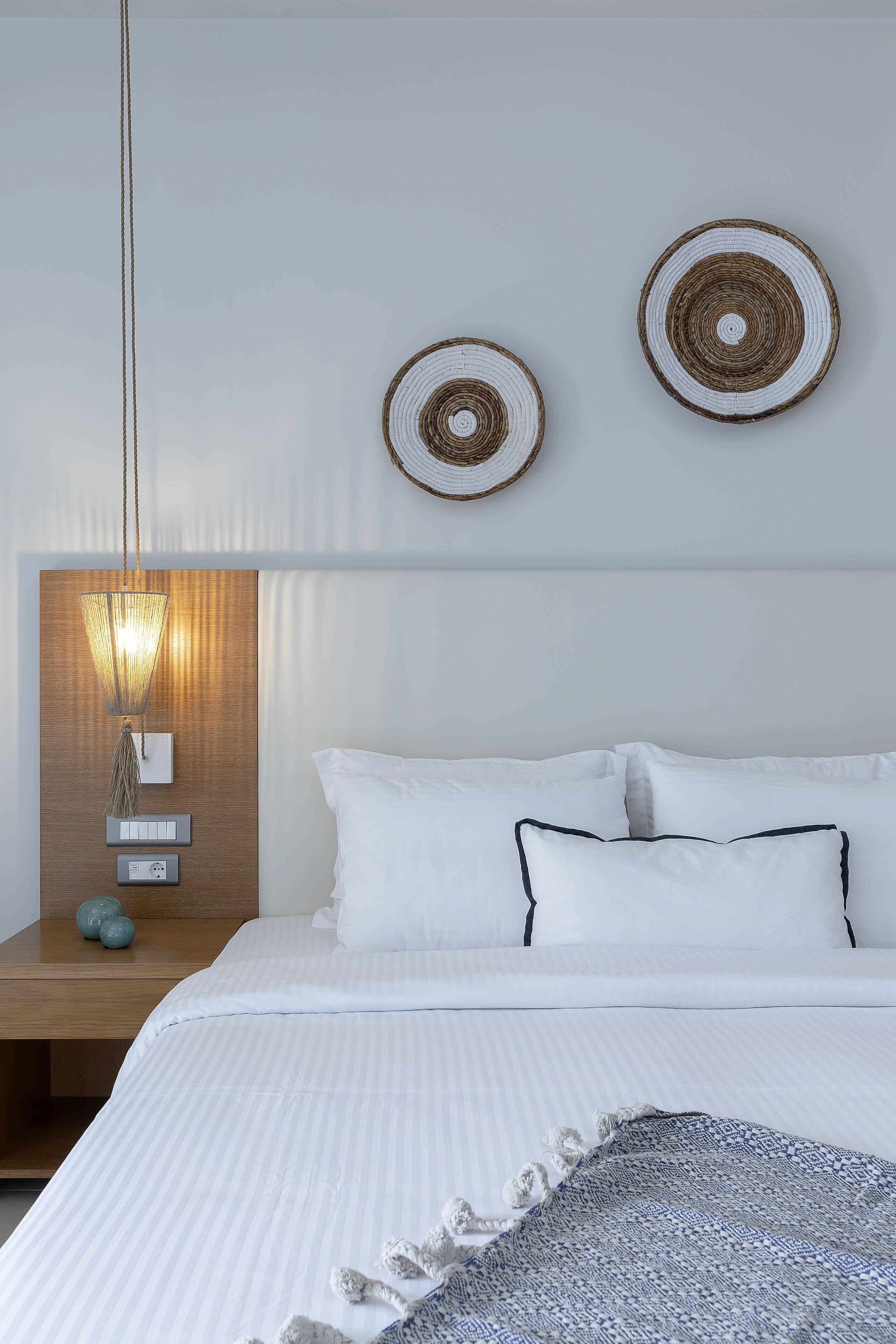 A modern bedroom with a wooden headboard, a bedside table with a lamp, and two wall-mounted decorative items.