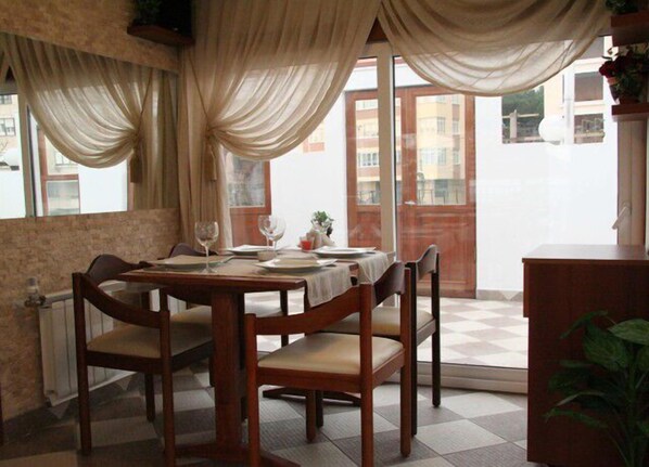 A dining area with a table set for two, wooden chairs, and a view through a glass door to the outside.