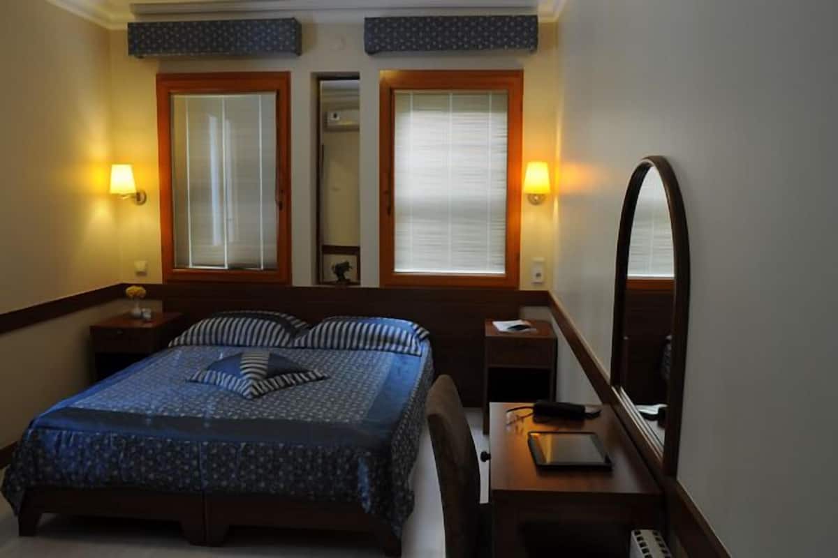 Ein Hotelzimmer mit Bett, Nachttischen, einem Spiegel und zwei Fenstern mit Jalousien.