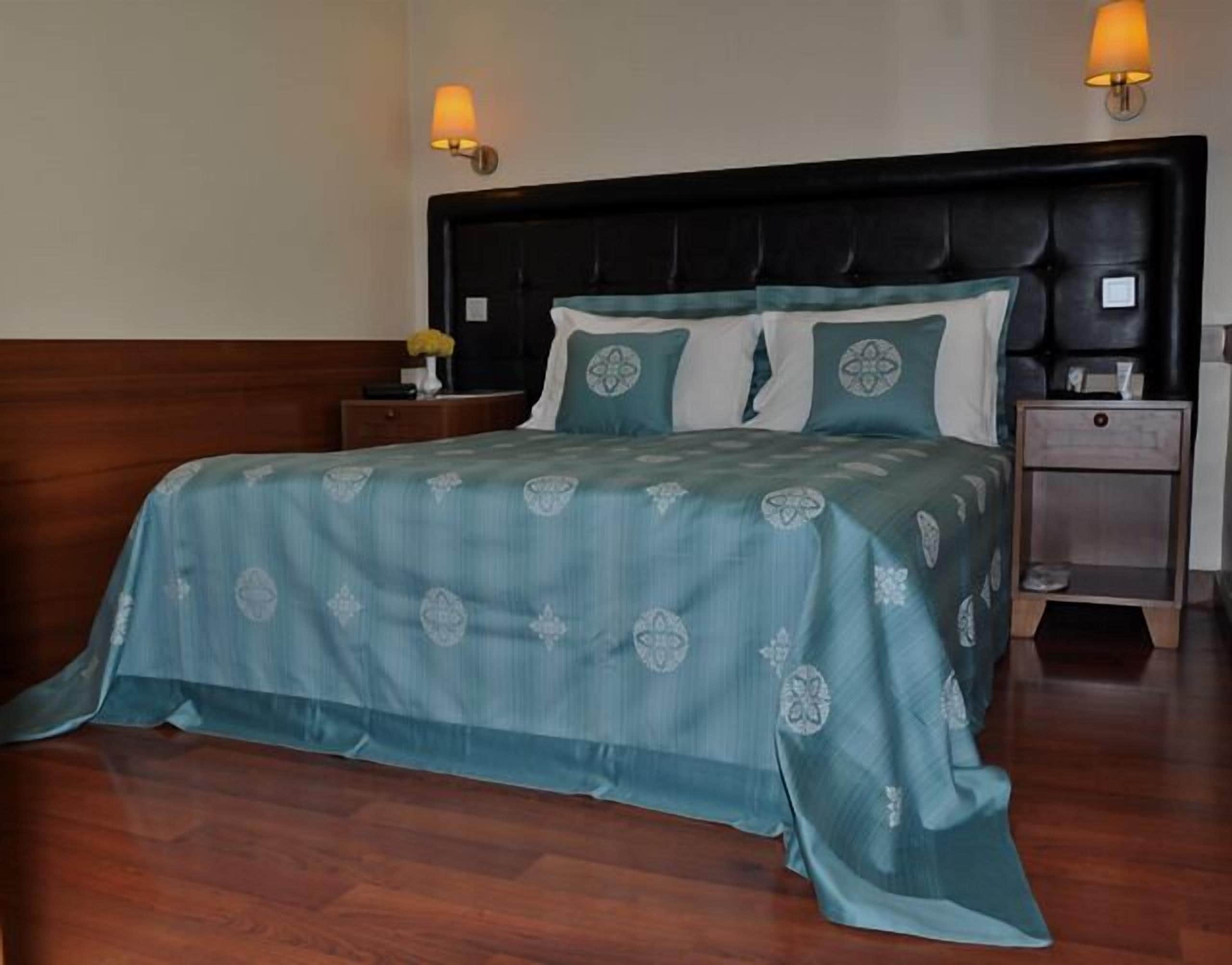 Un lit bien fait, avec une couvre-lit à motifs, une tête de lit sombre et deux lampes de chevet.