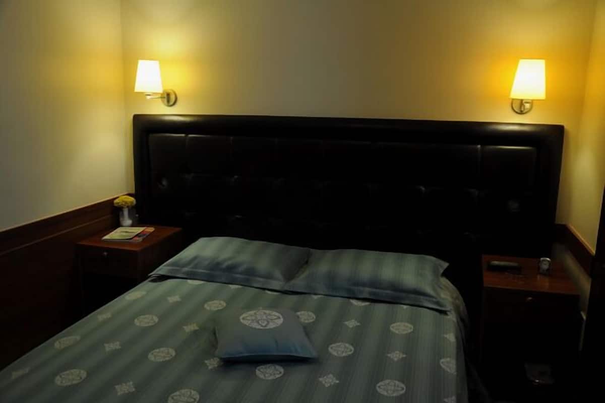 Ein Hotelzimmer mit einem Bett, zwei Nachttischlampen und einem Nachttisch mit einem Buch und einer Vase.