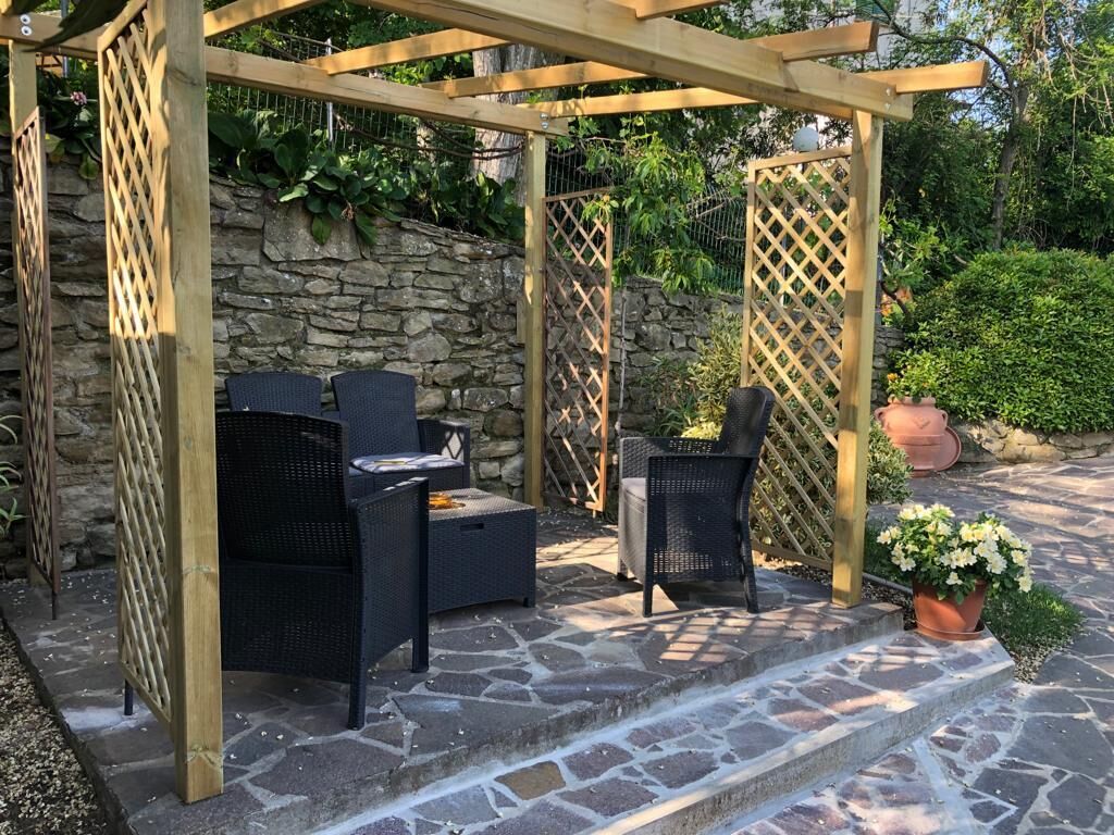 A wooden pergola with wicker furniture and a stone wall backdrop.