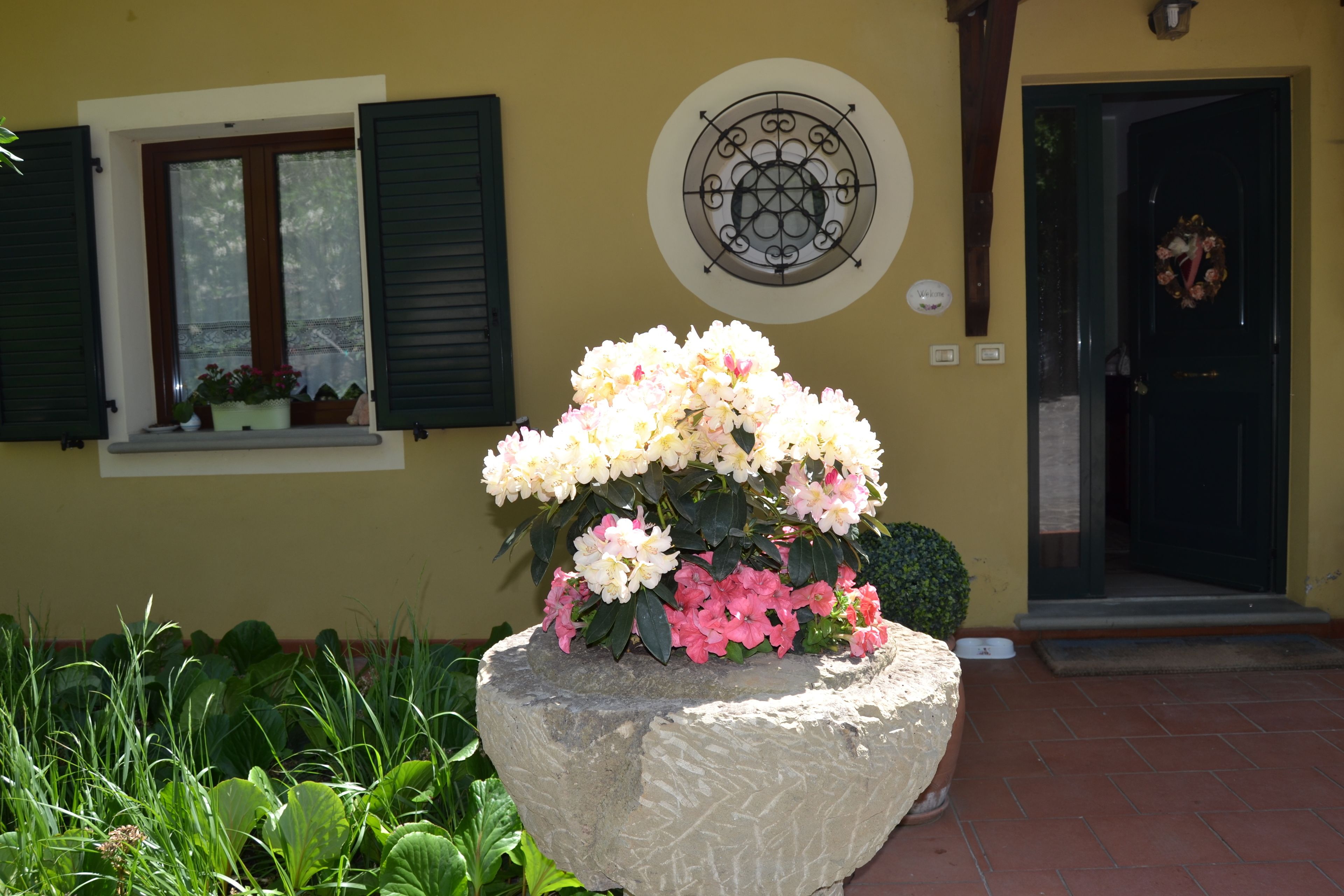 A stone planter with flowers in front of a building with a door and window.