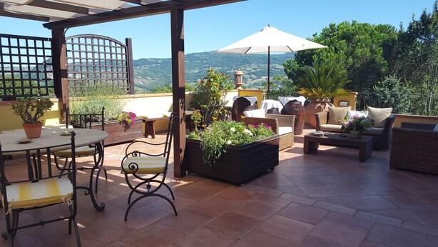 An outdoor patio with a table, chairs, and a sofa. There are potted plants and a wooden barrel. - Bed & Breakfast La Valle (Talamello)