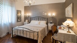 A bedroom with a bed, bedside tables, a chair, a table with a lamp, and a chandelier. - Bed & Breakfast La Valle (Talamello)