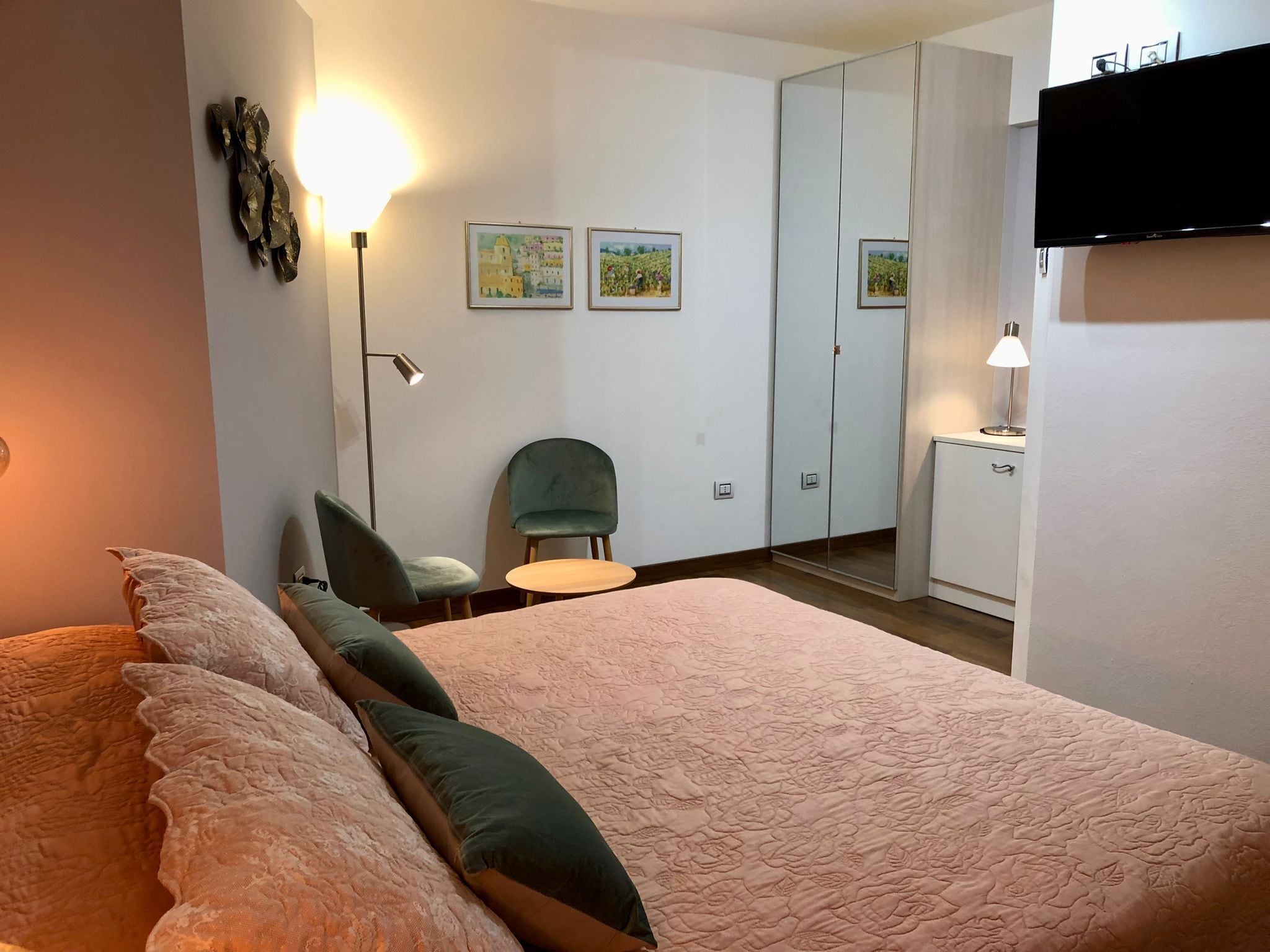 A bedroom with a large bed, a chair, a small table, a mirror, and a TV.