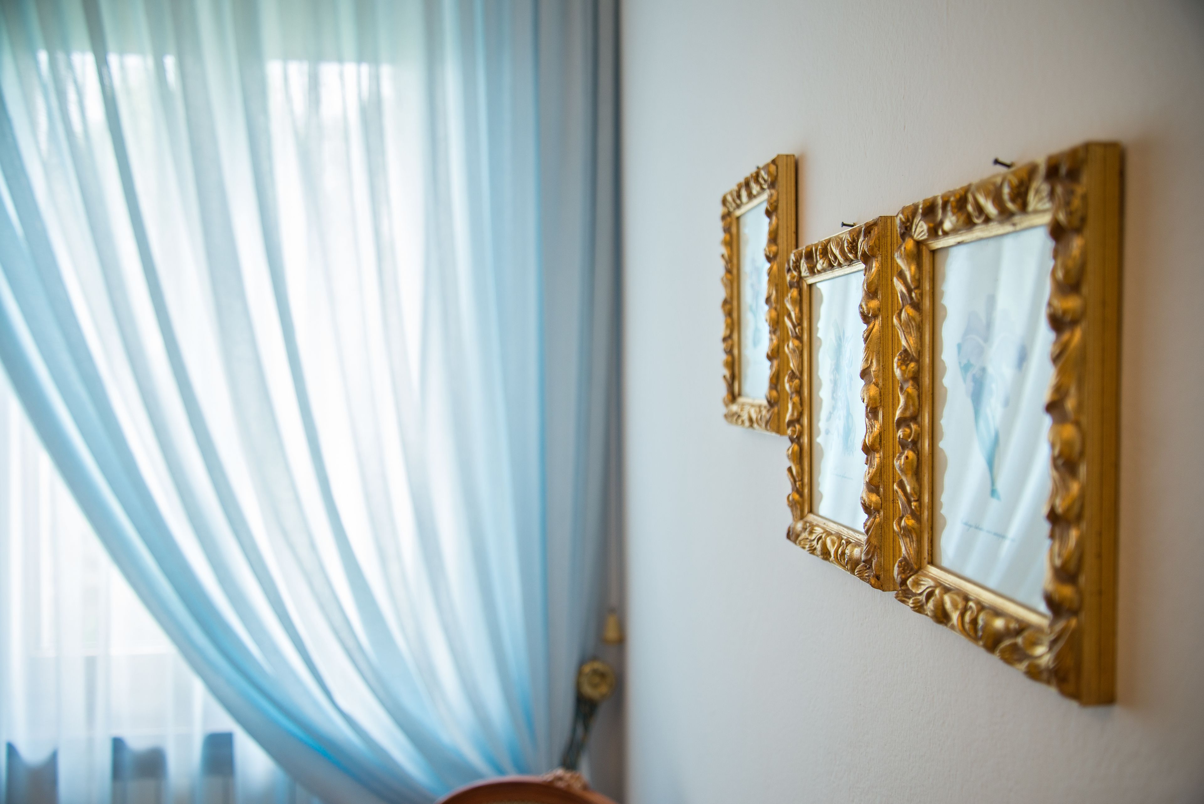 A room with a large window covered by sheer curtains, a wall-mounted ornate mirror, and a visible door handle.