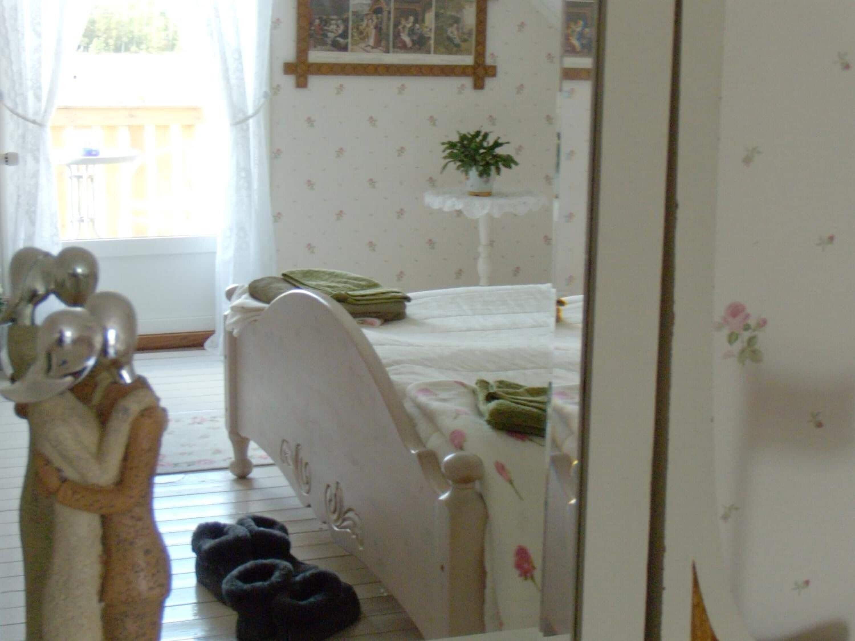 A bedroom with a bed, a bedside table with a plant, and a mirror.