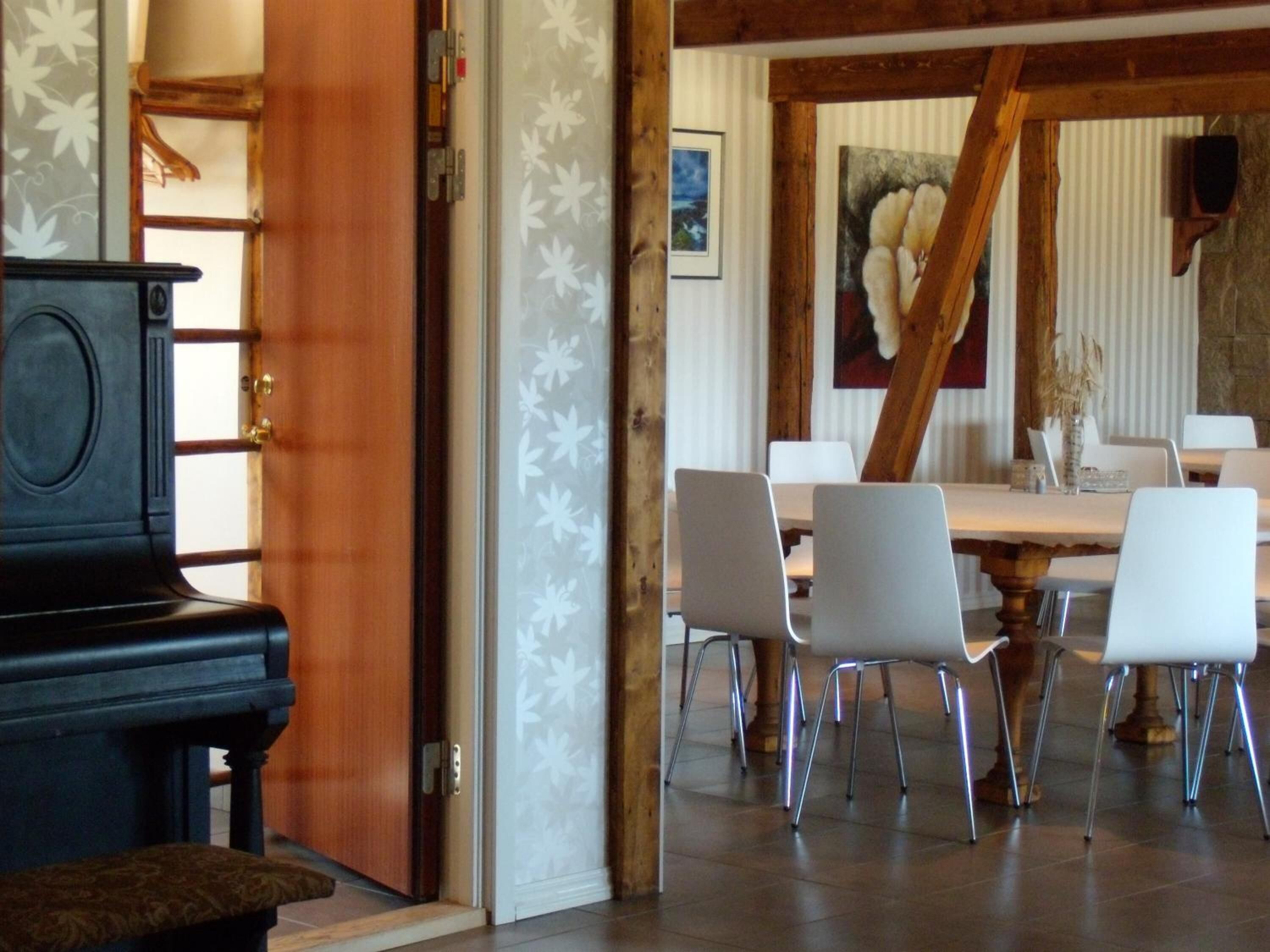 A dining area with a wooden table and white chairs, a piano, and a decorative wall with a floral pattern.