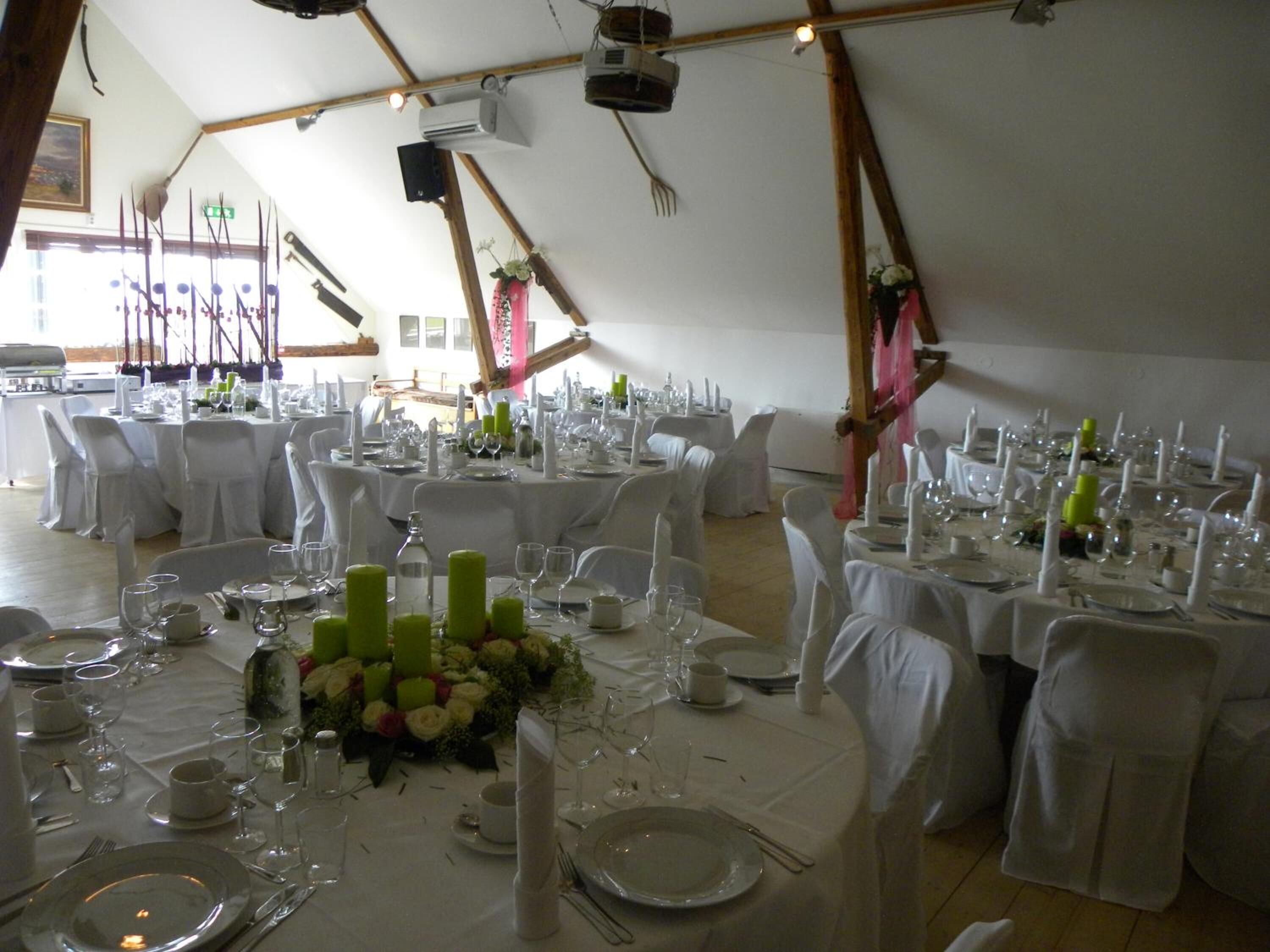 A banquet hall with round tables set for a formal event, featuring white tablecloths, green floral centerpieces, and white chairs.
