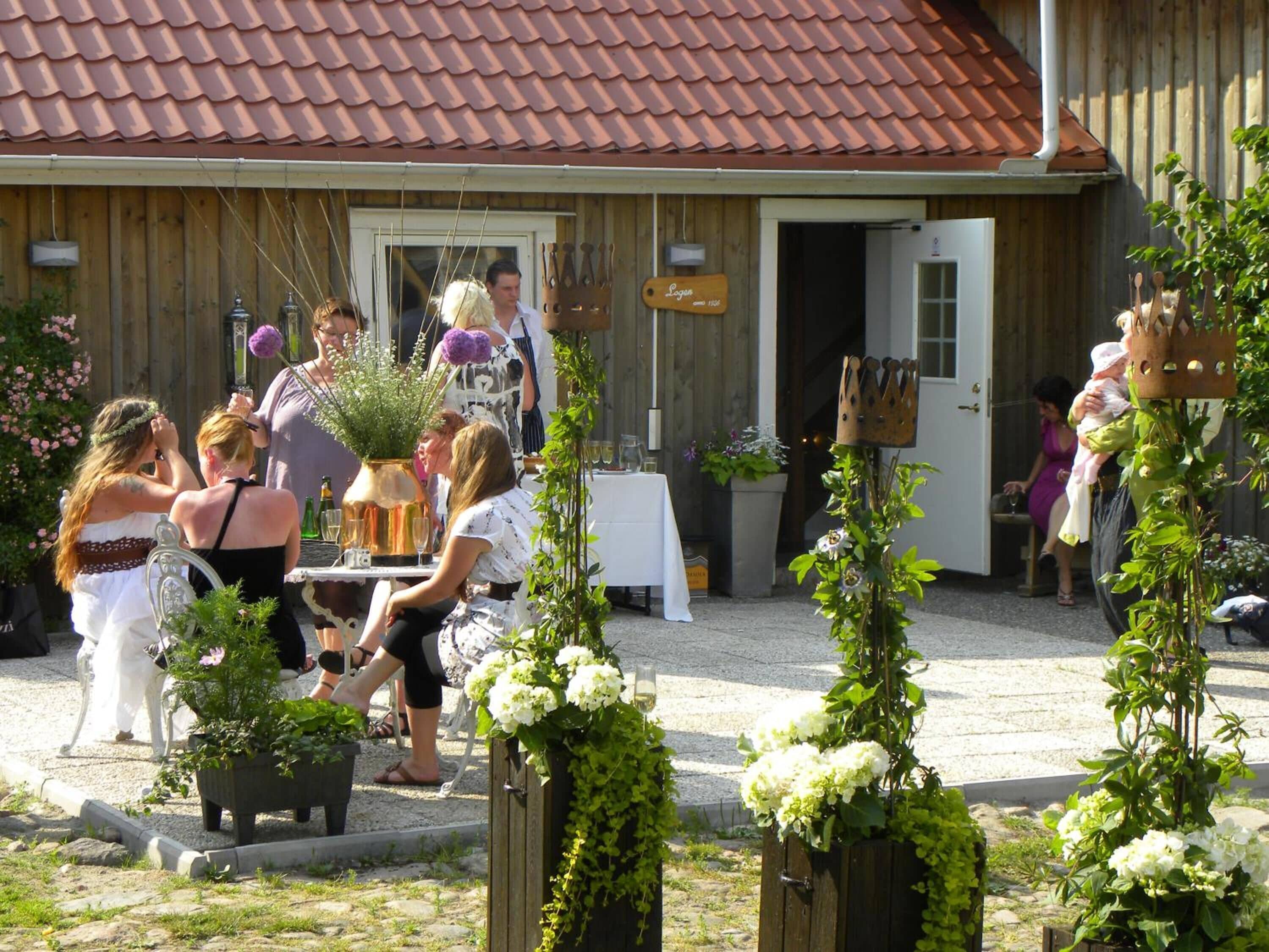 Et udendørs siddeområde med borde og stole, omgivet af plantekasser med blomster.