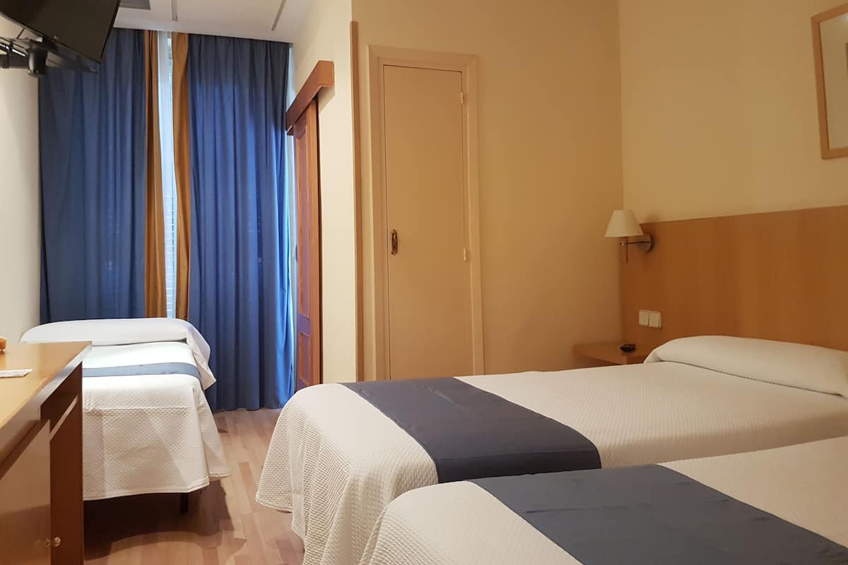 Une chambre d’hôtel avec deux lits, un bureau, une télévision et une porte.