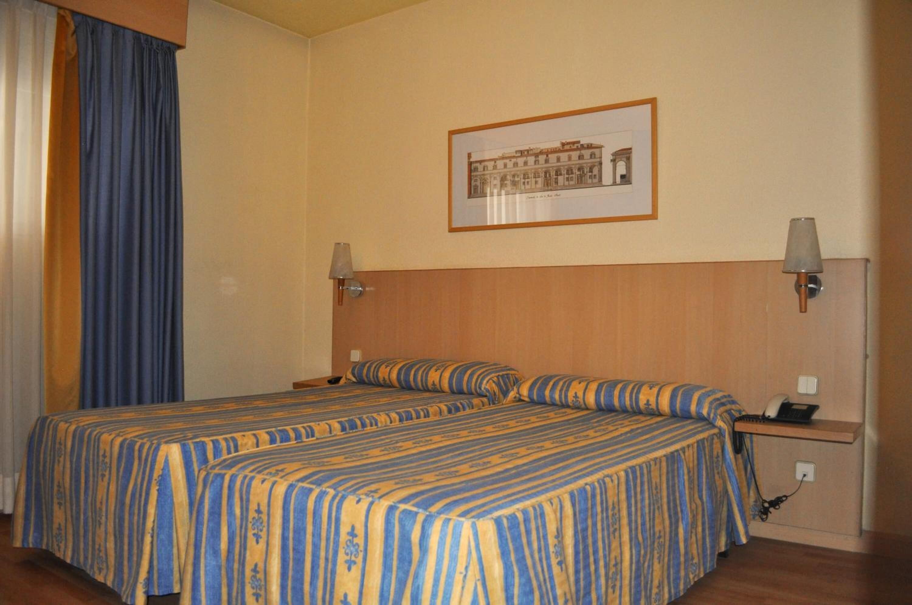Habitación de hotel con cama doble, dos mesitas de noche con lámparas, un cuadro enmarcado en la pared y un teléfono en la mesita de noche.