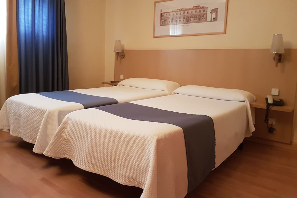 Un lit double avec une couvre-lit blanche et bleue, une table de chevet avec une lampe et un tableau encadré au mur.