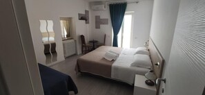 A hotel room with a bed, a small table, and a chair. There is a window with curtains and a view of the outside.