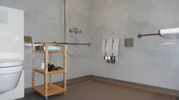 A bathroom with a toilet, a wooden shelf with toiletries, a towel rack, and a shower.