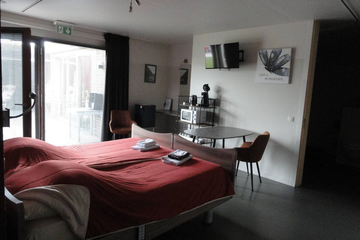 A hotel room with a bed, a desk, a chair, a television, and a window with blinds.