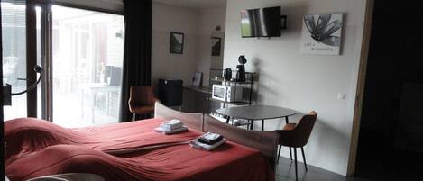 Een hotelkamer met een bed, een bureau, een stoel, een televisie en een raam met zonwering.