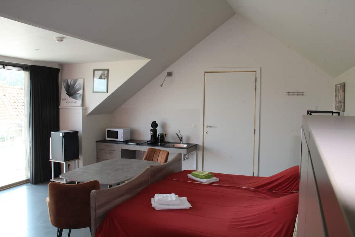 A bedroom with a bed, a desk, a chair, a microwave, and a window.