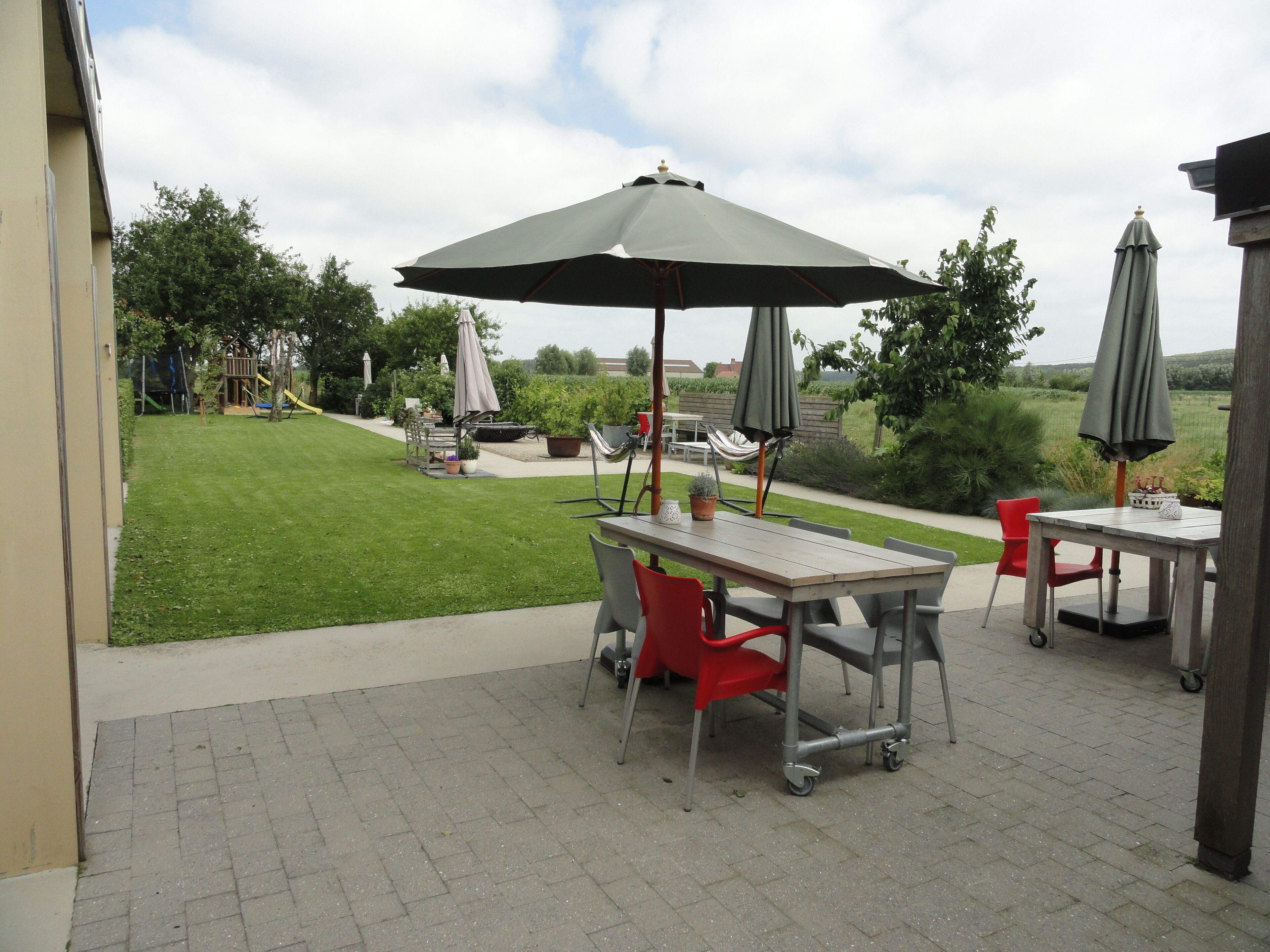 An outdoor patio area with a table and chairs, a swing set, and a grassy yard.
