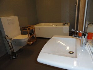 Un baño con inodoro, estante de madera, bañera y lavabo.