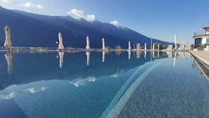 A clear swimming pool with a mountain backdrop, lounge chairs, and umbrellas along the poolside. - Hotel Mercedes (Limone sul Garda)
