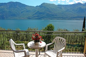 A balcony with two white chairs and a table with a flower arrangement, overlooking a lake and mountains. - Hotel Mercedes (Limone sul Garda)