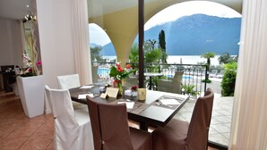 A dining area with a table set for four, a vase with flowers, and a view of a mountain and lake. - Hotel Mercedes (Limone sul Garda)