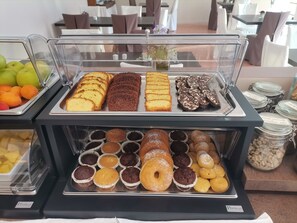 A buffet with various baked goods and pastries, including muffins, donuts, and bread.