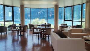 A spacious room with large windows offering a mountain view, furnished with a sofa, chairs, and tables. - Hotel Mercedes (Limone sul Garda)