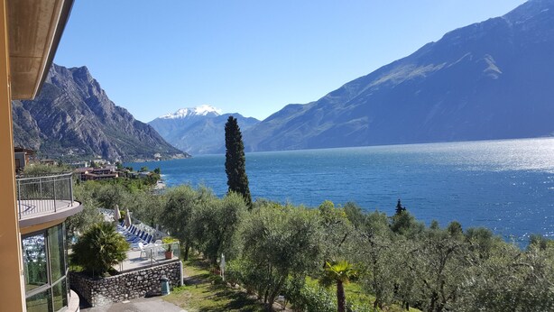 A balcony with outdoor seating overlooking a lake, surrounded by mountains and greenery. - Hotel Mercedes (Limone sul Garda)