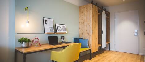 A modern office space with a wooden desk, a yellow chair, a laptop, and framed documents on the wall.