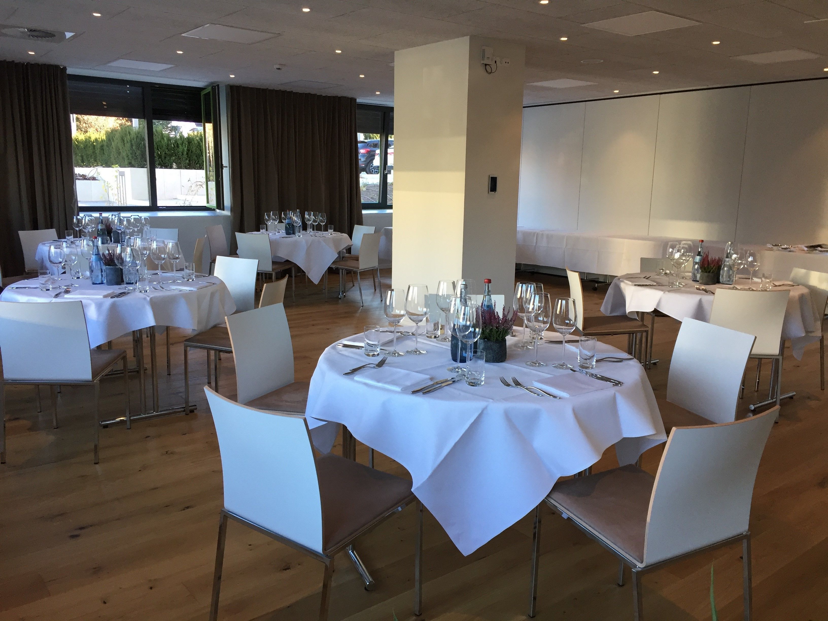 A restaurant with round tables set for dining, white tablecloths, and modern chairs.