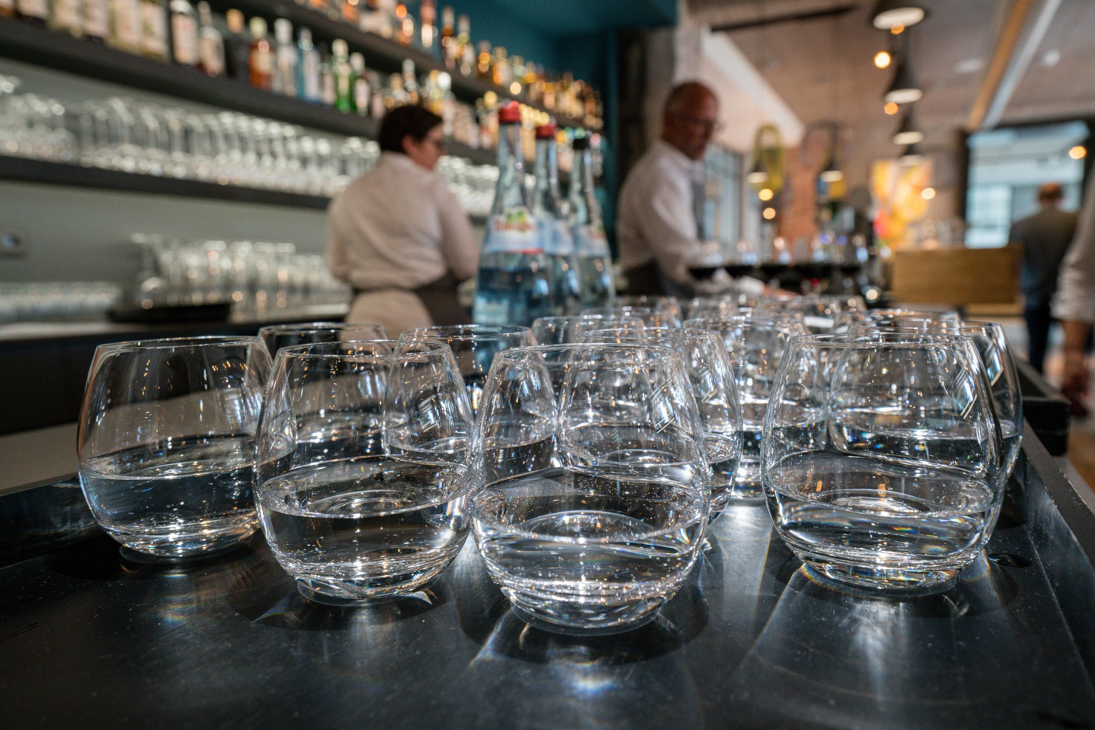 A bar area with multiple glasses of water and bottles of alcohol on shelves.