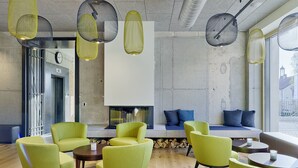 Un espace de détente moderne avec des fauteuils verts, une cheminée et des lampes suspendues.