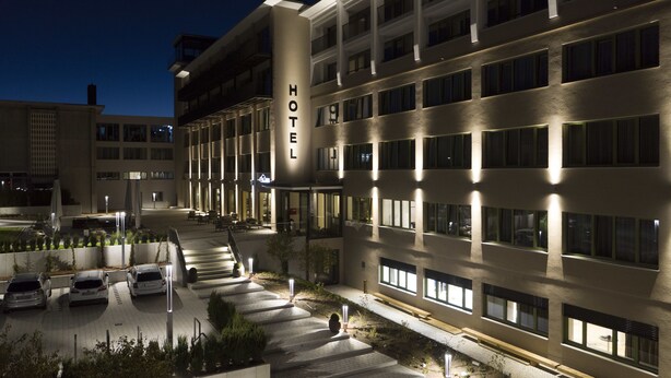 Un hôtel au design moderne, doté d’un escalier central menant à l’entrée, d’un parking pouvant accueillir plusieurs voitures et d’une façade bien éclairée.