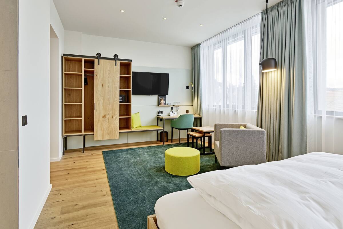 Una habitación de hotel moderna con cama, escritorio, silla, televisor y armario.