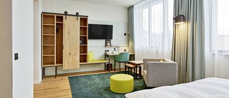 A modern hotel room with a bed, a desk, a chair, a TV, and a wardrobe.