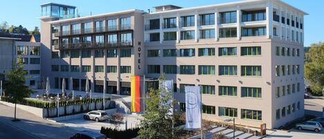 A modern hotel with multiple floors, large windows, and a rooftop terrace.