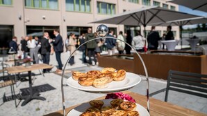 Un espace repas avec un présentoir à deux niveaux rempli de pâtisseries, des sièges en plein air et un bâtiment moderne en arrière-plan.