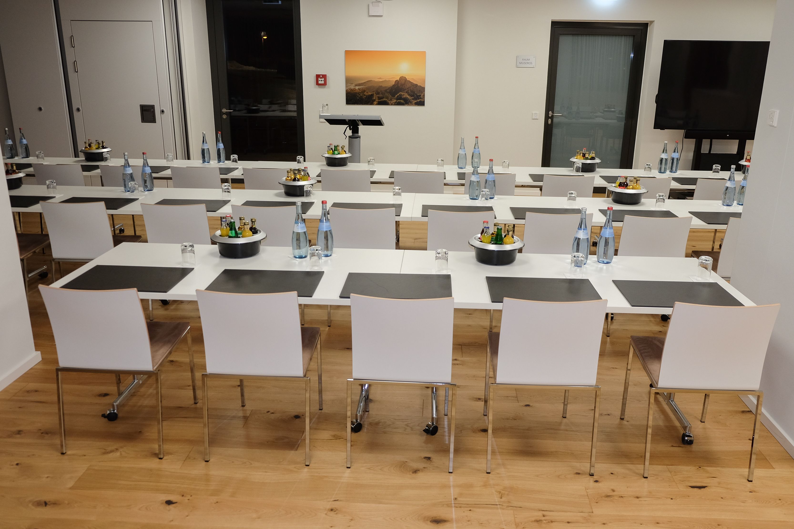 A conference room with multiple tables, chairs, and a large screen.