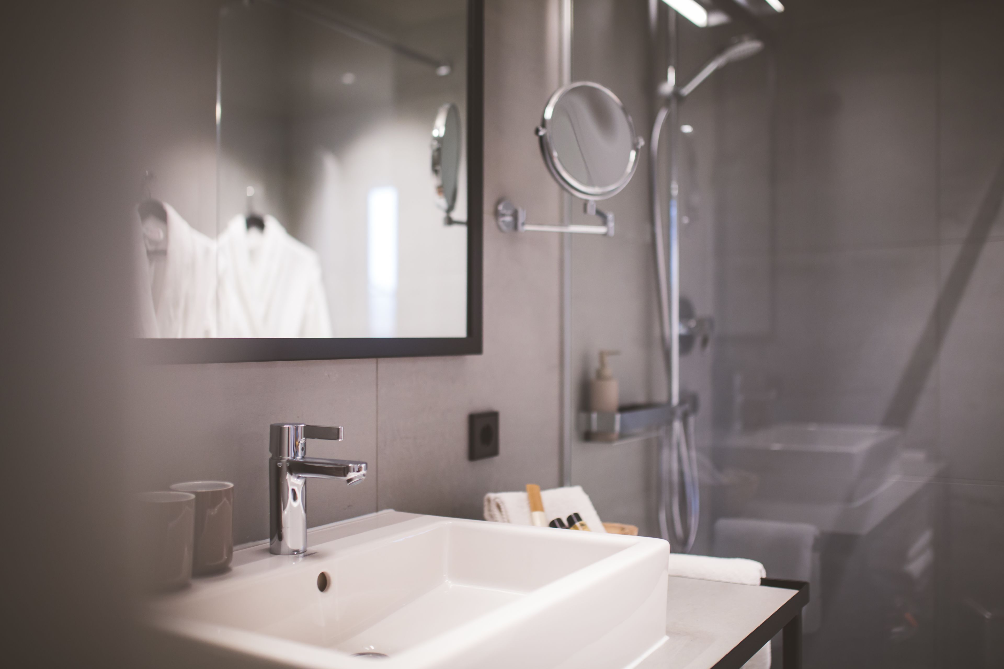 A modern bathroom with a large mirror, a white sink, and a shower area.