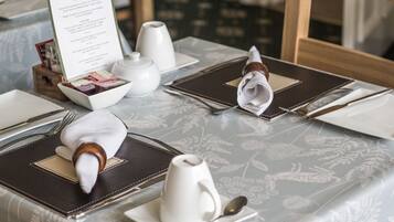 A breakfast setting with a menu, white teapots, a folded napkin, and a spoon on a table with a floral tablecloth.