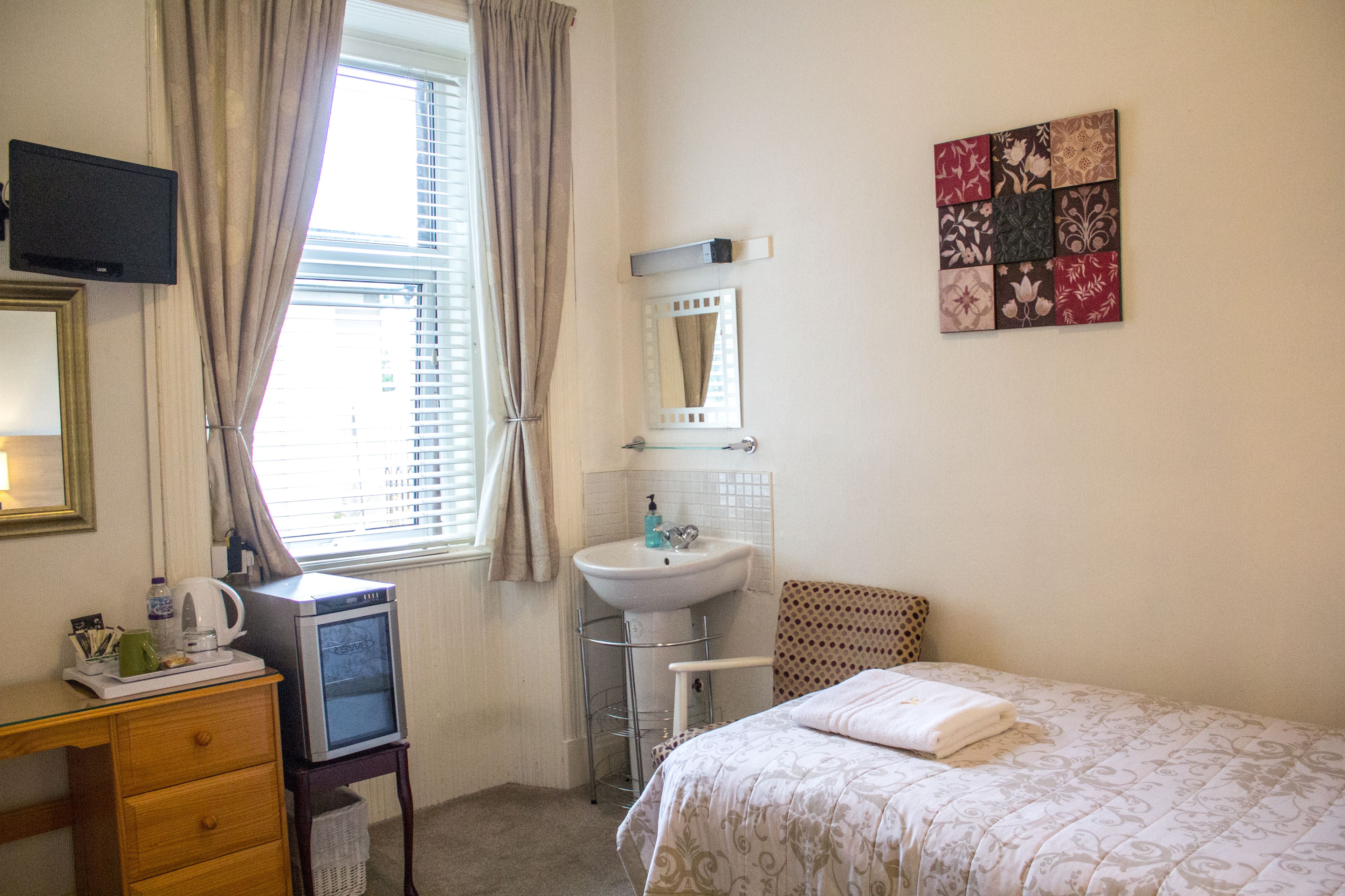 A hotel room with a bed, a desk with a television, a sink, and a window with curtains.