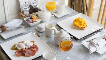 Una mesa de desayuno con platos de huevos y tostadas, un vaso de jugo de naranja y una taza de té.
