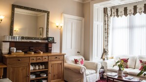 A well-lit living room with a wooden cabinet, a white sofa, and a large mirror. - Hazeldene Guest House (Perth)