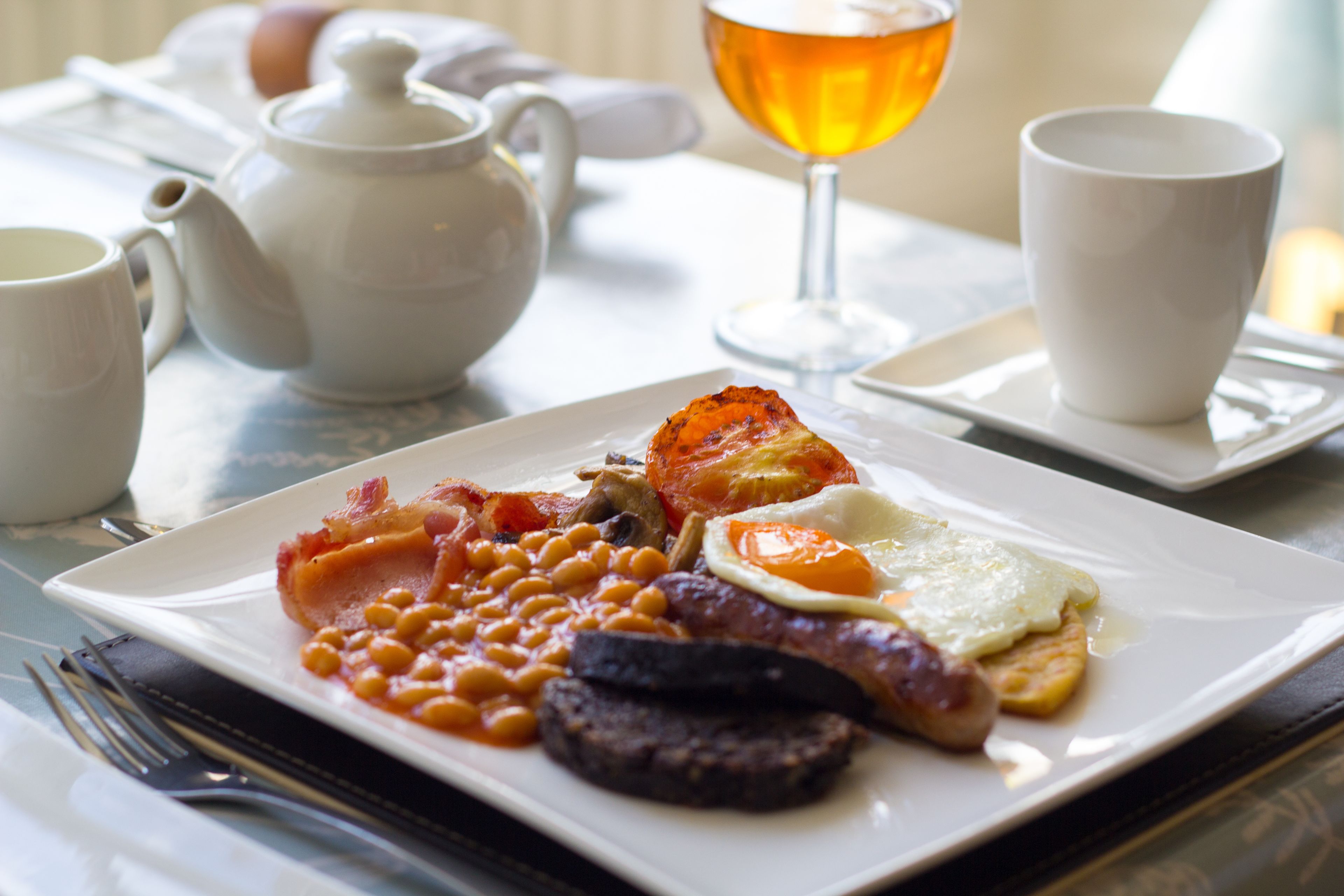 A breakfast plate with beans, bacon, sausage, and eggs.