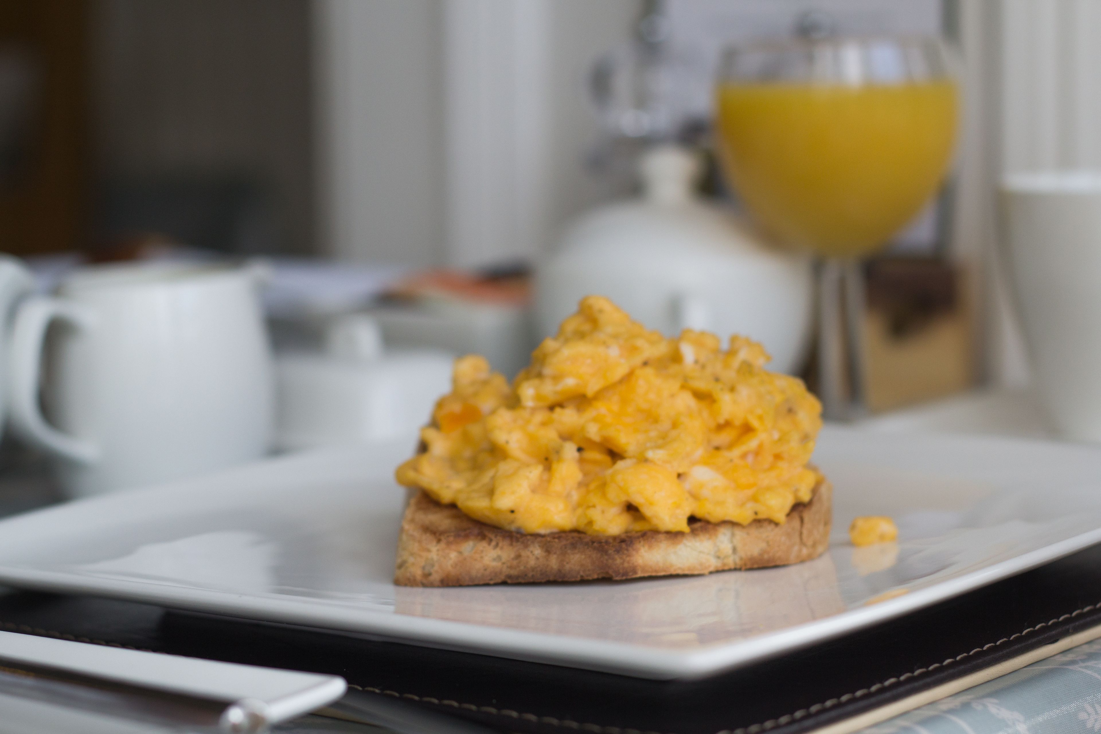 Huevos revueltos sobre tostada, con un vaso de zumo de naranja al fondo.